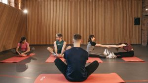 A group of adults practicing yoga and stretching on mats in a wooden panelled room.